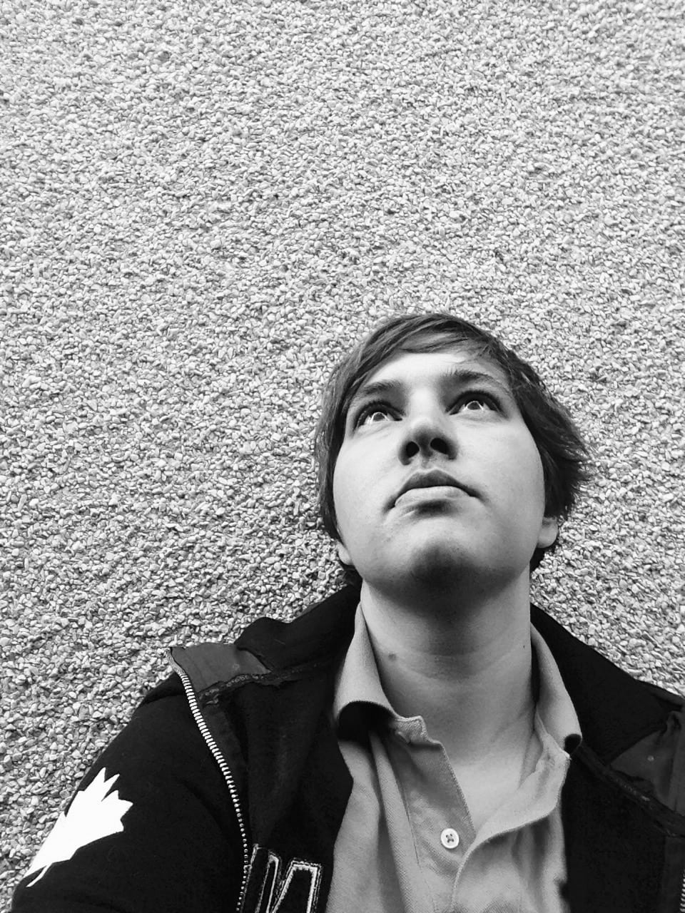 a black and white image of Alex Leslie in front of a stucco wall, shot from below.
