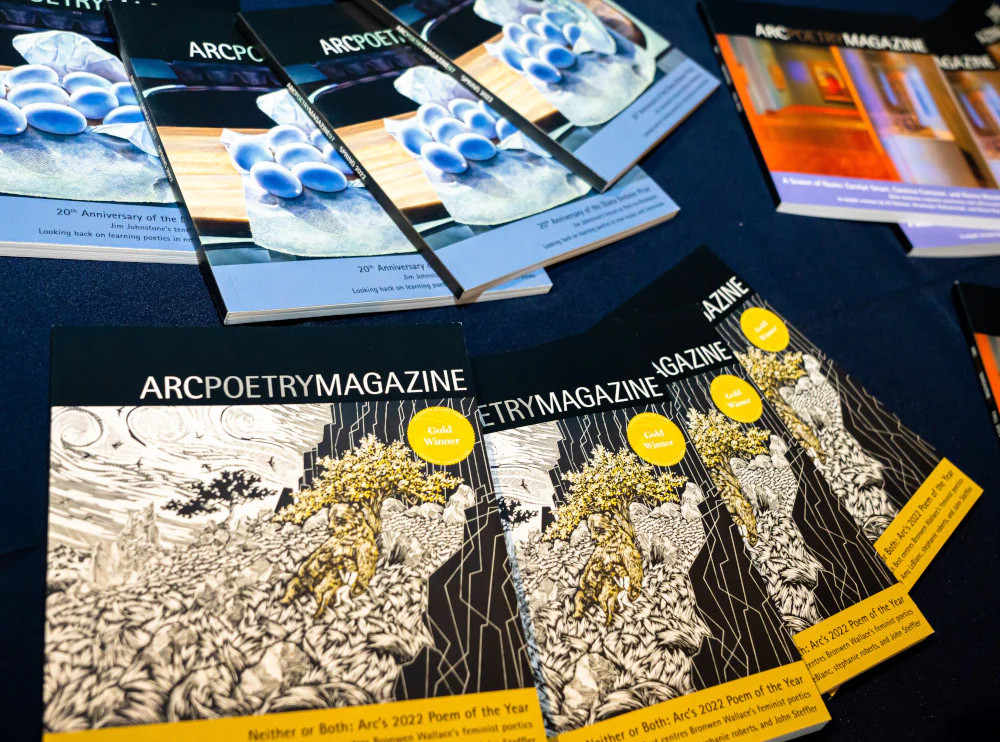 a table at a small press book fair, with a black tablecloth and with multiple copies of three recent issues of Arc Poetry Magazine
