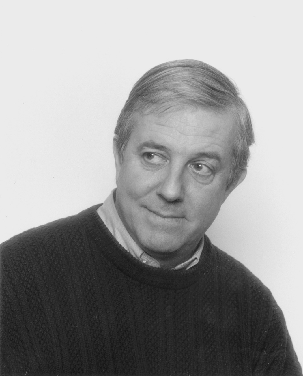 a black and white image of Mark Frutkin in a sweater and collard shirt, looking off to the side.